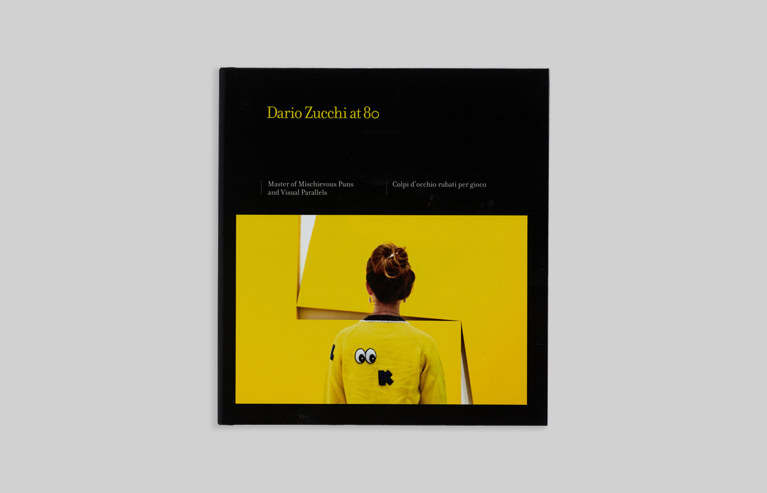 Zucchi photo on the cover has a figure wearing a yellow sweater standing in front of a yellow artwork with offset pieces.