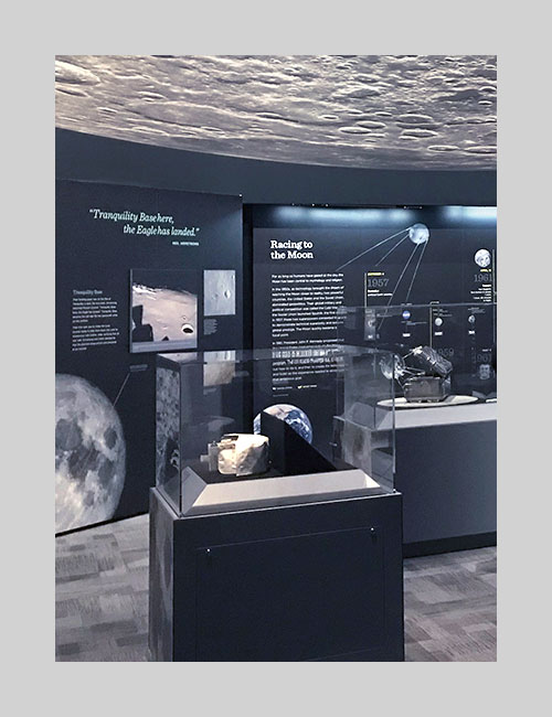 Exhibition photo of Destination Moon for SITES showing panels in the background and two object cases in the foreground.